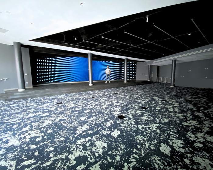 large arena style room with a stage, large colorful screen, and a man on stage in front of the screen